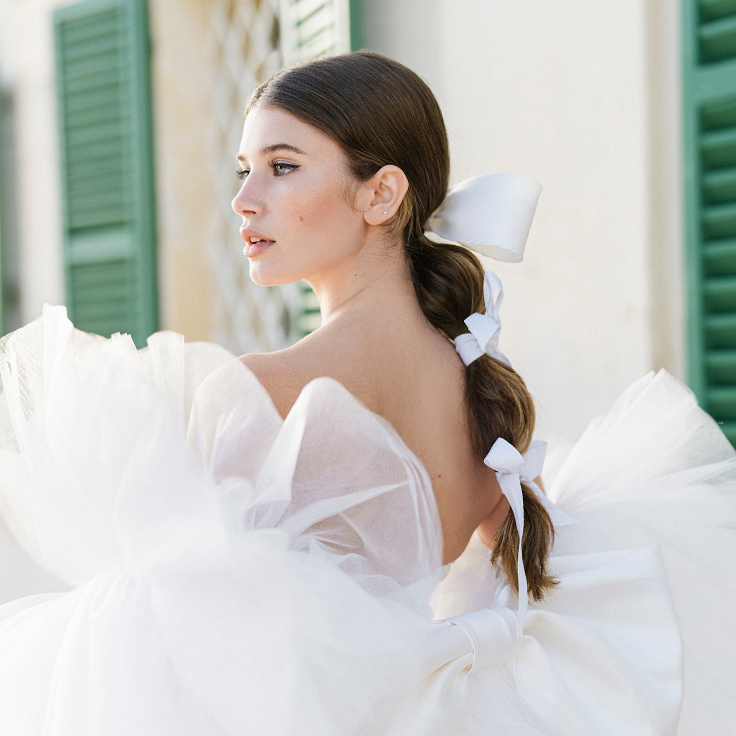 bride with a bubble ponytail in front of green windows