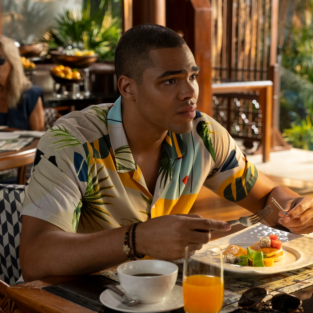 A man (Nicholas Duvernay as Zion) eats breakfast in a hotel dining room, in 'The White Lotus' season 3.